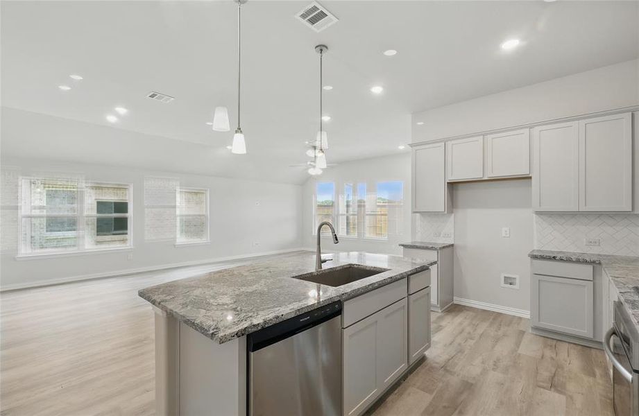 Kitchen with a kitchen island with sink, stainless steel appliances, backsplash, light stone countertops, and light wood-style floors Kitchen with a kitchen island with sink, stainless steel appliances, backsplash, light stone countertops, and light wood-style floors
