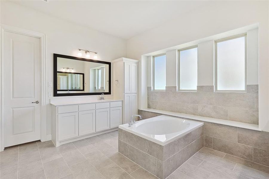 Bathroom featuring tile patterned flooring, vanity, and a relaxing tiled tub