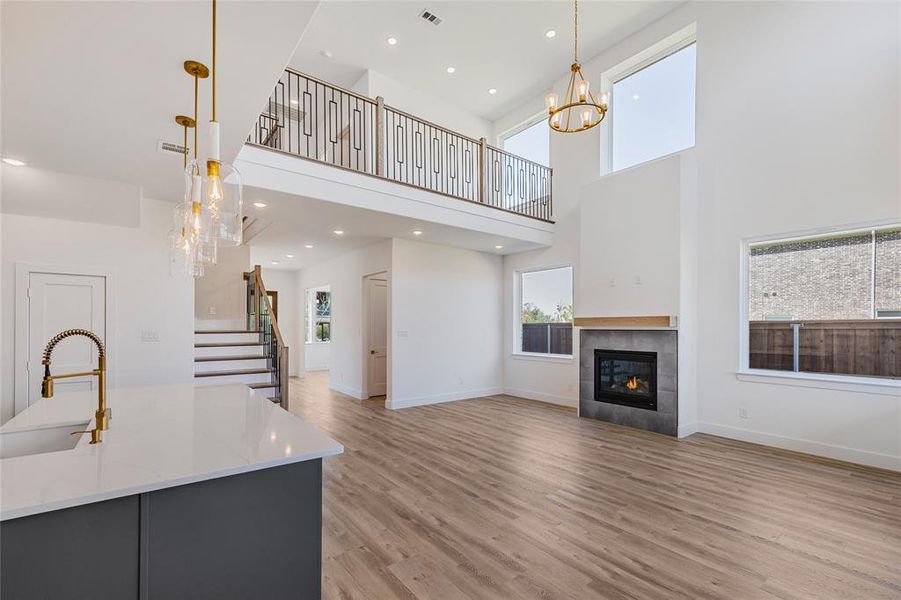 Unfurnished living room with a tile fireplace, sink, light hardwood / wood-style flooring, and a towering ceiling