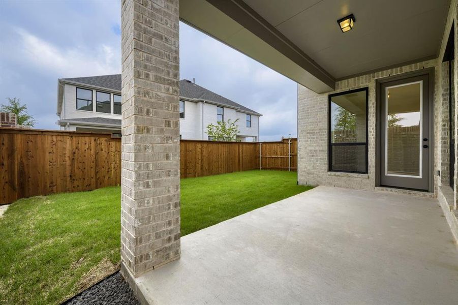 Covered concrete patio with a brick column and exterior wall, featuring a glass-paned door and large window Covered concrete patio with a brick column and exterior wall, featuring a glass-paned door and large window