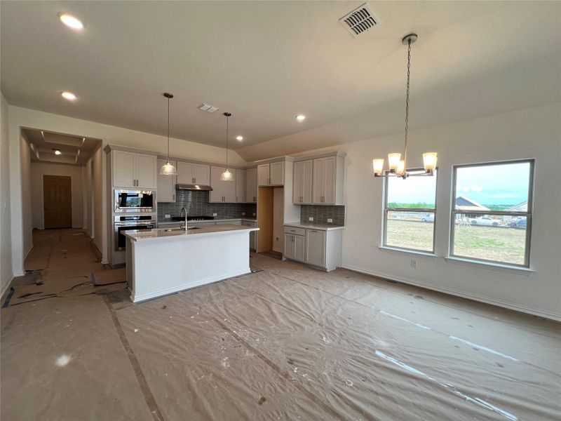 Kitchen with stainless steel appliances, backsplash, under cabinet range hood, a center island with sink, and a chandelier Kitchen with stainless steel appliances, backsplash, under cabinet range hood, a center island with sink, and a chandelier