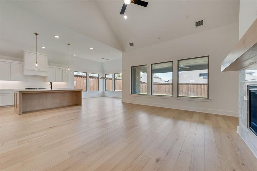 Unfurnished living room featuring high vaulted ceiling, recessed lighting, a tiled fireplace, light wood-style flooring, and a ceiling fan