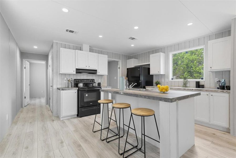 Kitchen with white cabinets, black appliances, a breakfast bar, recessed lighting, and a center island with sink Kitchen with white cabinets, black appliances, a breakfast bar, recessed lighting, and a center island with sink
