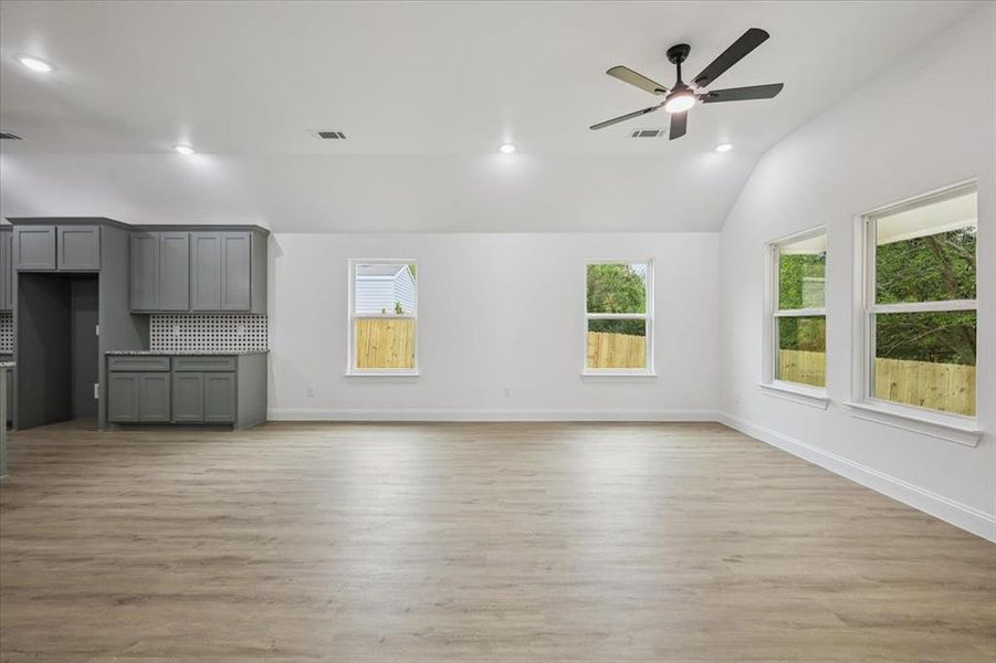 Unfurnished living room featuring light wood-style floors, plenty of natural light, recessed lighting, vaulted ceiling, and a ceiling fan Unfurnished living room featuring light wood-style floors, plenty of natural light, recessed lighting, vaulted ceiling, and a ceiling fan