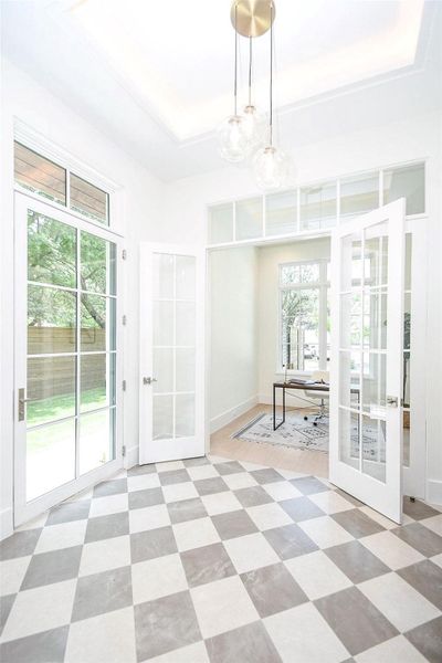 Bright entryway with checkered flooring, large glass doors, and an elegant pendant light. Adjacent room offers a cozy office space with ample natural light.