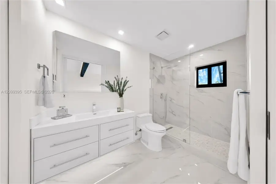 Bathroom featuring a white floating dual-drawer vanity with an integrated sink, floor-to-ceiling stone-style tile shower surround with a glass enclosure, and stone-style flooring