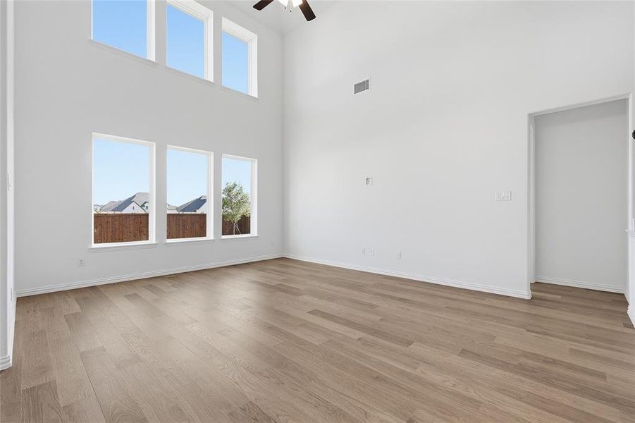Empty room with a high ceiling, healthy amount of natural light, ceiling fan, and light wood-type flooring