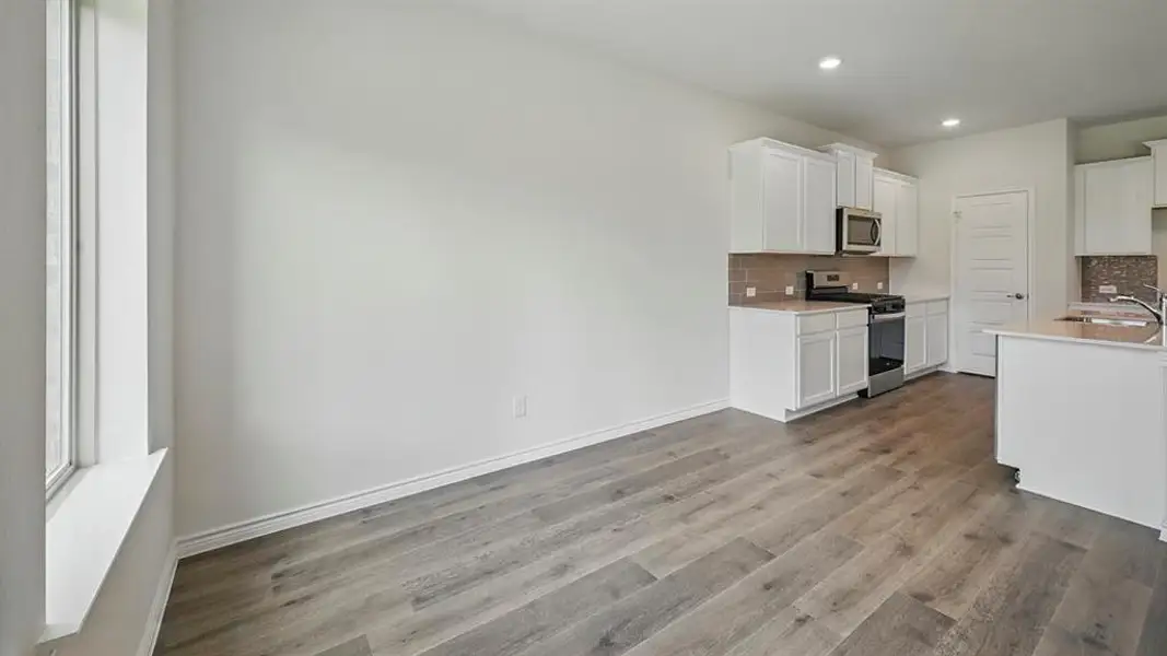 Open-concept kitchen and dining area featuring wood-finish flooring, white cabinetry, stainless steel appliances, a tile backsplash, and an island with a sink Open-concept kitchen and dining area featuring wood-finish flooring, white cabinetry, stainless steel appliances, a tile backsplash, and an island with a sink