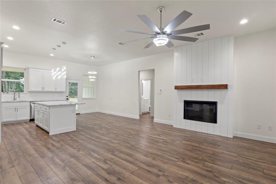Open-concept living area featuring a fireplace with a wood mantel, wood-finish flooring, and a modern ceiling fan Open-concept living area featuring a fireplace with a wood mantel, wood-finish flooring, and a modern ceiling fan