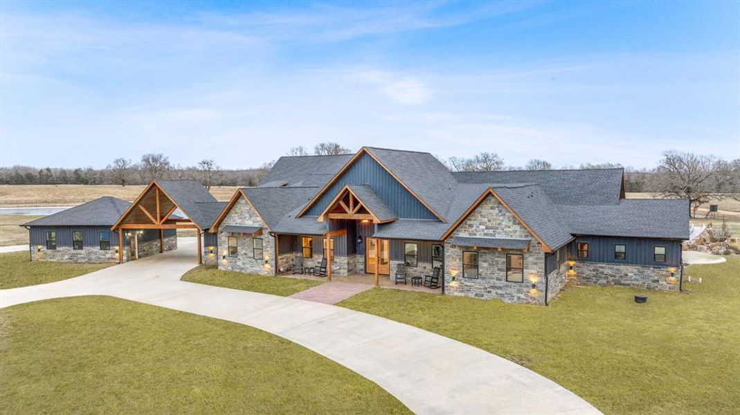 View of front of property with stone siding, driveway, an attached carport, a front yard, and covered porch