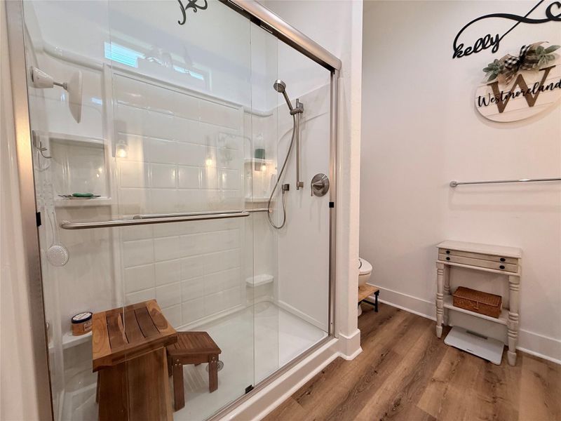 This bathroom features a modern walk-in shower with glass doors, wood accents, and sleek fixtures. The space is bright and inviting with stylish decor and wooden flooring, offering a cozy and functional design.