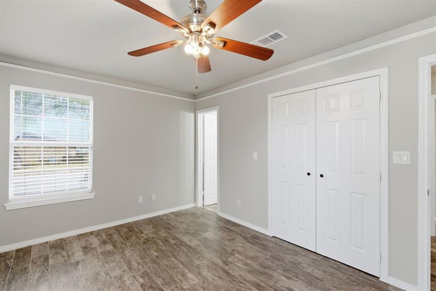 Unfurnished bedroom with wood finished floors, a closet, a ceiling fan, and ornamental molding Unfurnished bedroom with wood finished floors, a closet, a ceiling fan, and ornamental molding