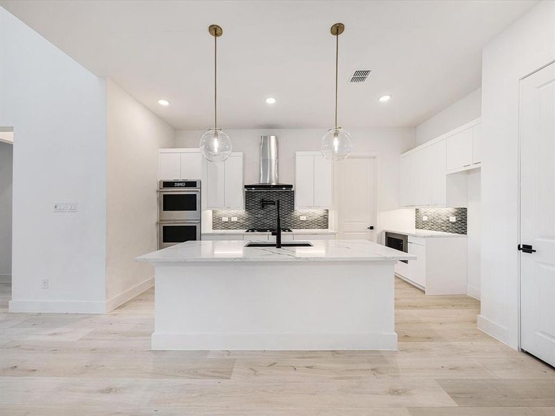 Kitchen with white cabinetry, light stone counters, decorative light fixtures, light wood-type flooring, and stainless steel double oven