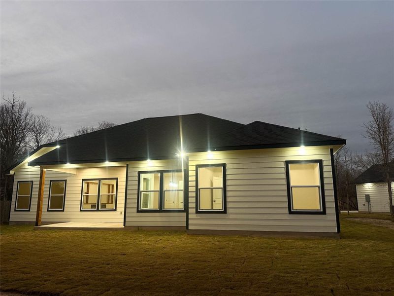 Rear view of house with a lawn, roof with shingles, and a patio area