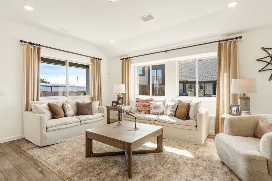 Bright living room with two white sofas, wood coffee table, and large windows with tan curtains