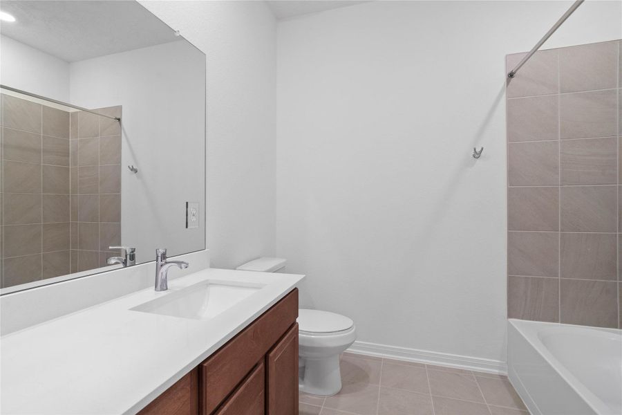 Well-appointed secondary bath with tub/shower combination and tile surround. It also features an extended vanity with a light countertop and a mirror that extends the full length of the vanity.