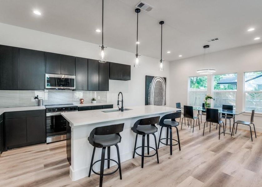 Kitchen with appliances with stainless steel finishes, light hardwood / wood-style flooring, sink, decorative light fixtures, and decorative backsplash