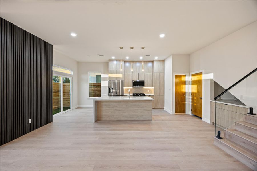 Kitchen with modern cabinets, an island with sink, decorative light fixtures, appliances with stainless steel finishes, and light wood-style flooring