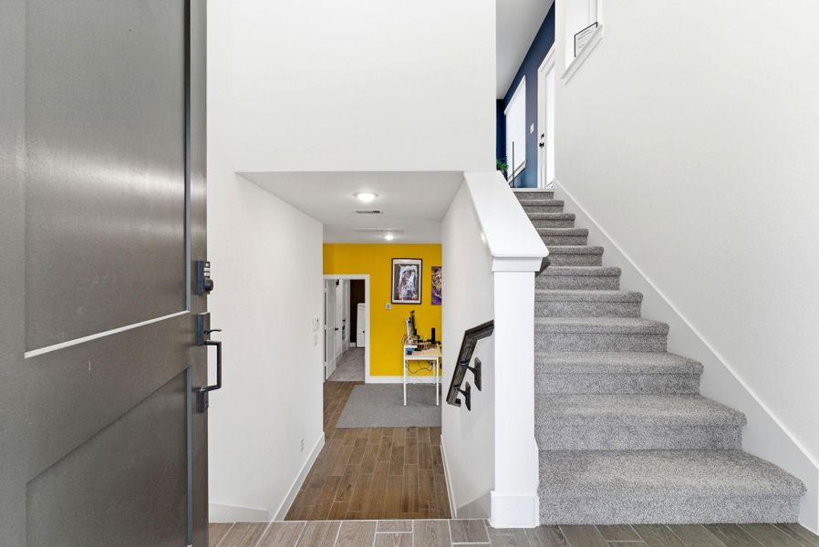 Bright entryway with wood-look tile flooring and an open staircase that sets the tone for the home’s modern interior.