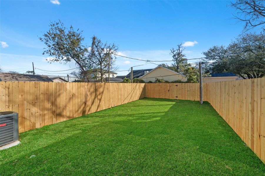 This photo features a spacious backyard with well-maintained green grass, enclosed by a wooden privacy fence. The area is clear and open, ideal for outdoor activities or gardening.