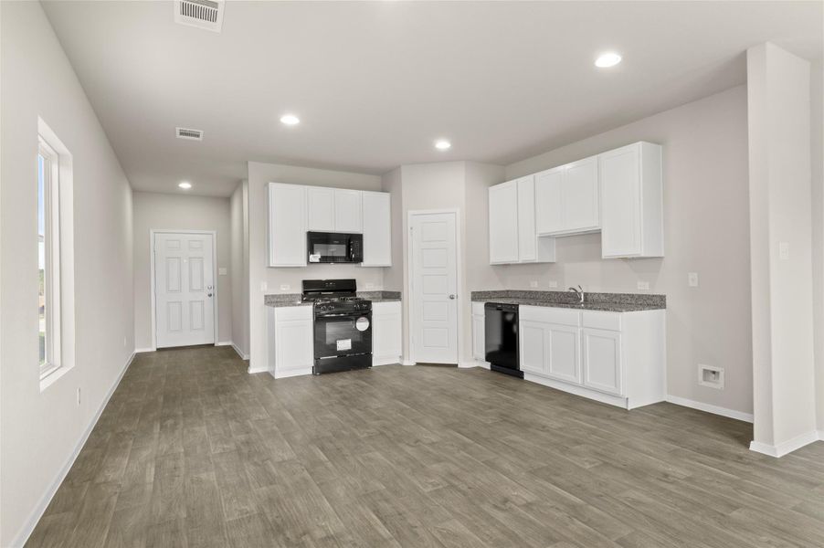 Kitchen with black appliances, recessed lighting, wood finished floors, white cabinetry, and dark stone counters