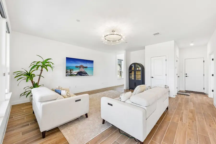 Natural light illuminates rich wood flooring and a modern chandelier, creating an inviting living space.