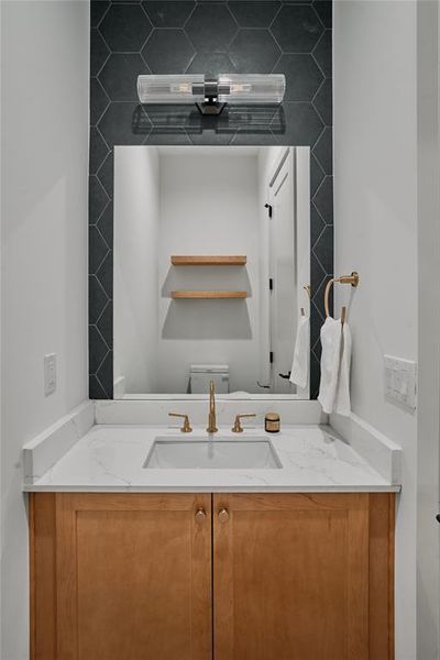 Vanity featuring a light wood-finish cabinet with gold-tone hardware, a white countertop, and an undermount sink with a gold-tone faucet