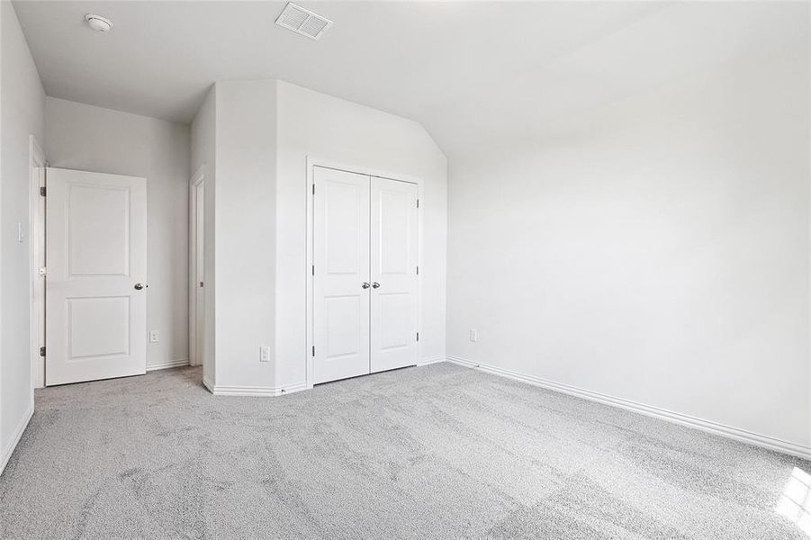 Unfurnished bedroom featuring light carpet, a closet, and lofted ceiling