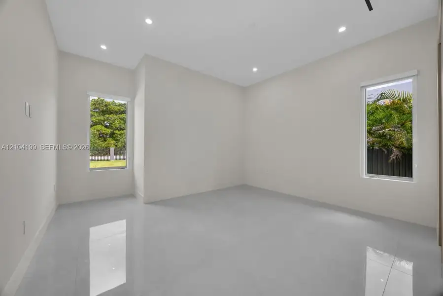 Neutral-toned interior room featuring large-format tile flooring, recessed ceiling lighting, and two windows providing natural illumination