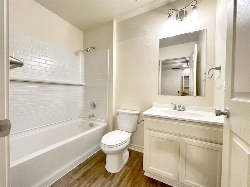 Bathroom featuring dark wood-style flooring, bathtub / shower combination, vanity, and a textured wall
