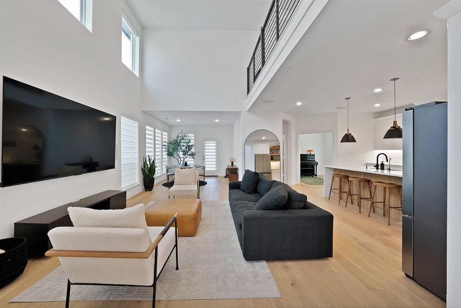Spacious open-concept living area featuring high ceilings, light wood-finish flooring, and multiple large windows with horizontal blinds