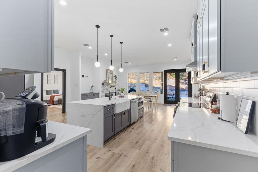 Kitchen with light stone countertops, gray cabinets, a kitchen island with sink, light wood-style floors, and decorative light fixtures