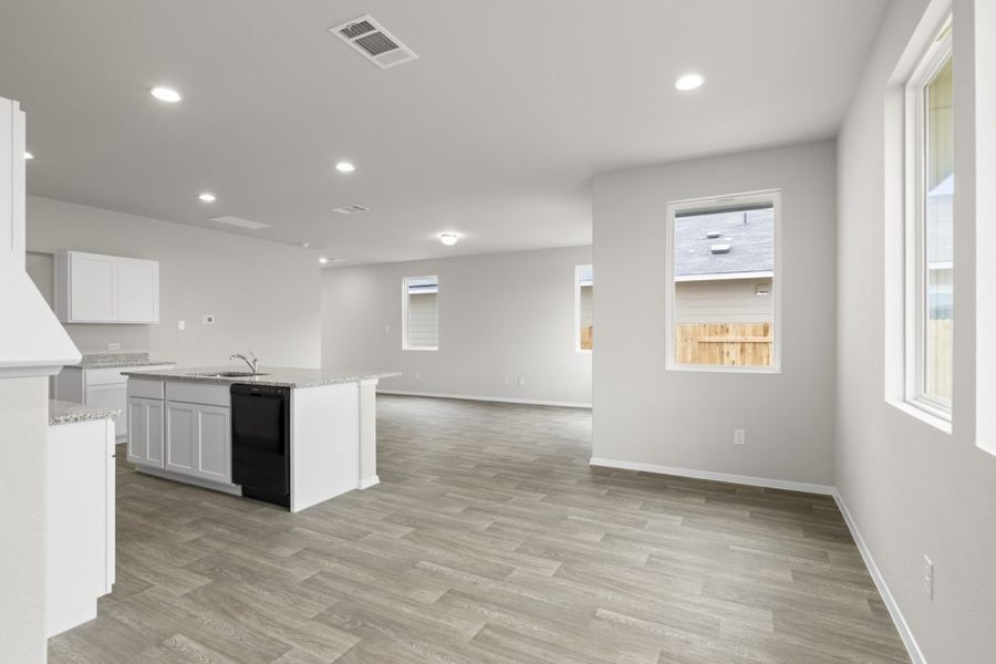 Image of a dining room area with a kitchen to the lest, cream walls, light brown flooring and windows