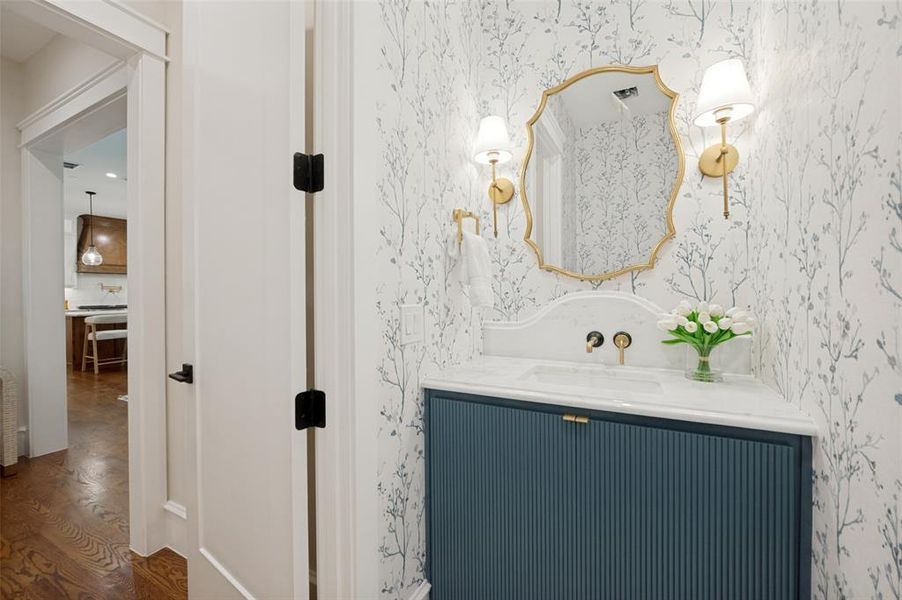 Powder room with botanical-patterned wallpaper, a gold-framed mirror, and brass sconces