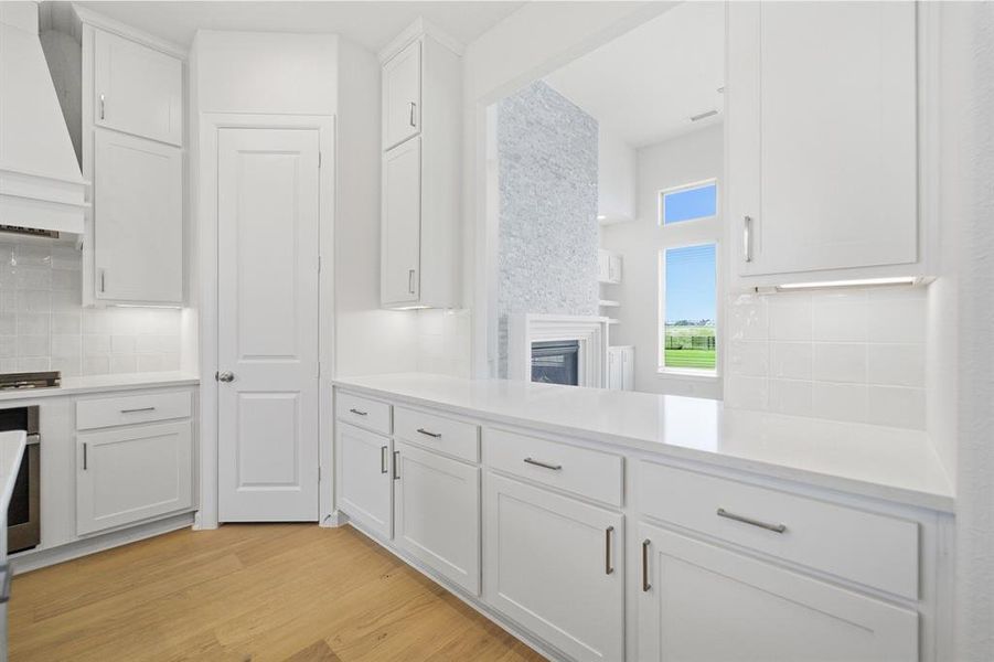 White kitchen cabinetry with sleek hardware, light wood-finish flooring, and subway tile backsplash