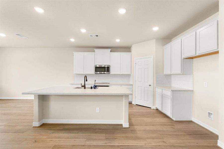 This light and bright kitchen features a large quartz island, white cabinets, a large sink overlooking your family room, recessed lighting, and beautiful backsplash.