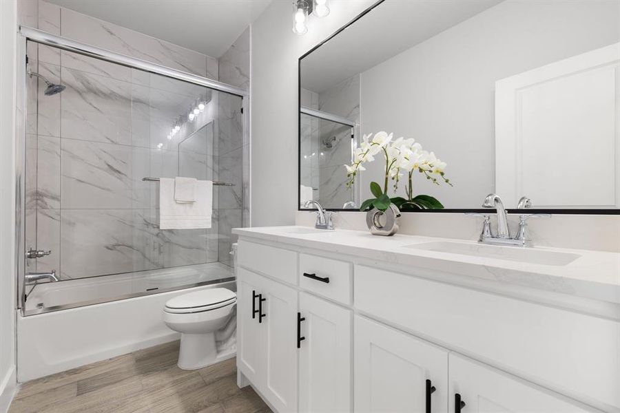 Bathroom with toilet, bath / shower combo with glass door, wood finished floors, a sink, and double vanity