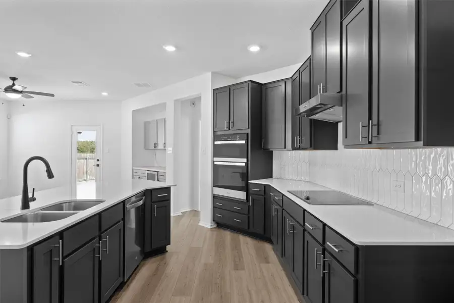 Kitchen featuring dark cabinets, a center island with sink, light wood-style floors, decorative backsplash, and recessed lighting