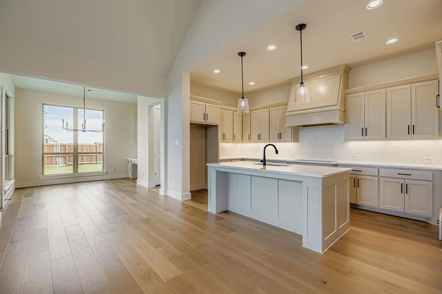 Kitchen with tasteful backsplash, hanging light fixtures, a kitchen island with sink, light wood finished floors, and a kitchen breakfast bar Kitchen with tasteful backsplash, hanging light fixtures, a kitchen island with sink, light wood finished floors, and a kitchen breakfast bar