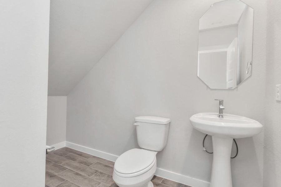 This half bathroom features a stylish pedestal sink, modern hardware, and bright recessed lighting, creating a sleek and inviting space. Sample photo of completed home with similar floor plan. Actual colors and selections may vary.