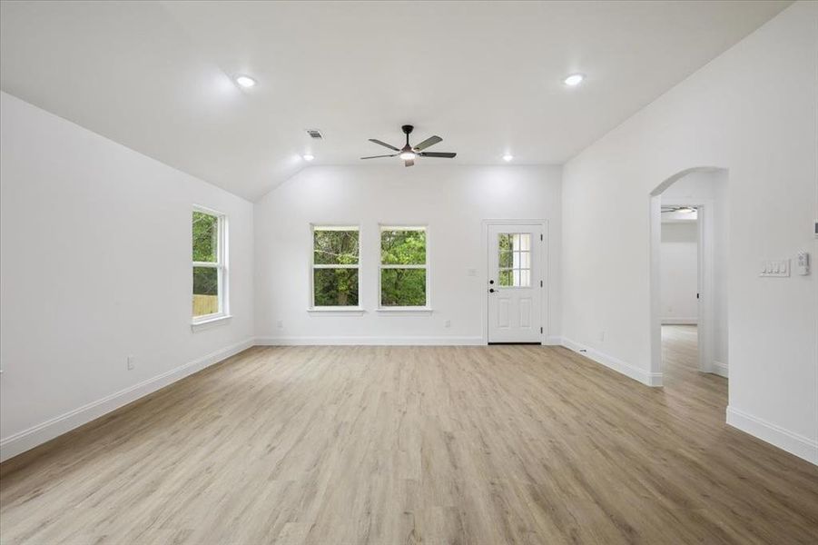 Unfurnished living room with arched walkways, light wood-style floors, recessed lighting, lofted ceiling, and a ceiling fan Unfurnished living room with arched walkways, light wood-style floors, recessed lighting, lofted ceiling, and a ceiling fan