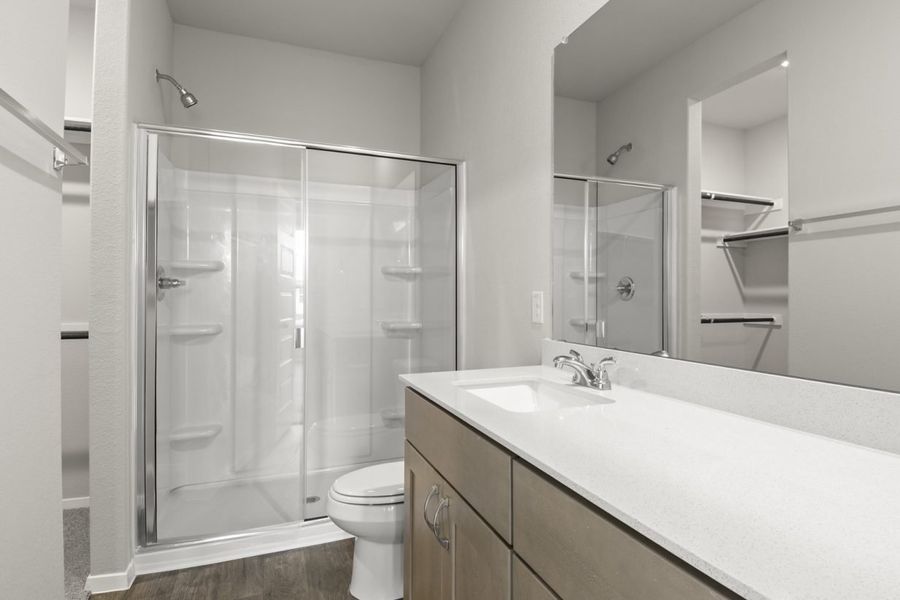 Image of primary bathroom with a walk in shower and brown cabinets and a mirror with a white counter vanity Image of primary bathroom with a walk in shower and brown cabinets and a mirror with a white counter vanity