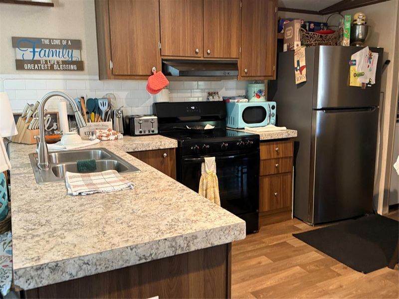 Kitchen featuring black / electric stove, light countertops, freestanding refrigerator, and wood finish cabinets