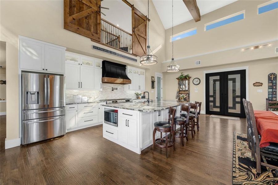 Kitchen with stainless steel fridge with ice dispenser, white cabinetry, a high ceiling, glass insert cabinets, and hanging light fixtures