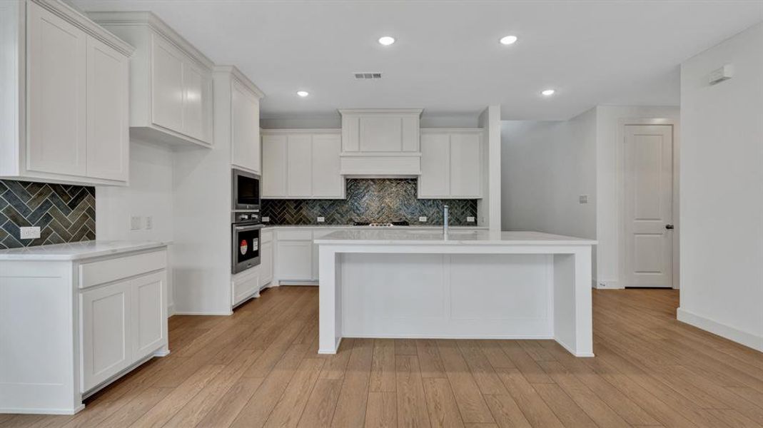 Kitchen featuring oven, white cabinetry, built in microwave, and an island with sink