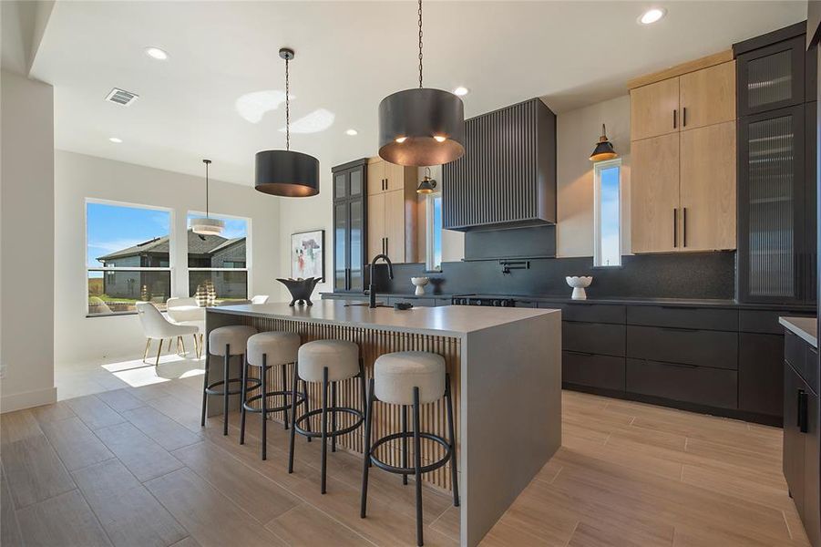 Kitchen featuring glass insert cabinets, light brown cabinets, a breakfast bar, ventilation hood, and recessed lighting Kitchen featuring glass insert cabinets, light brown cabinets, a breakfast bar, ventilation hood, and recessed lighting