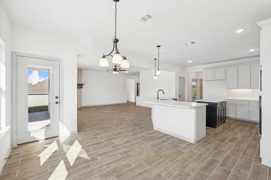 Kitchen with a kitchen island with sink, hanging light fixtures, and light wood-type flooring