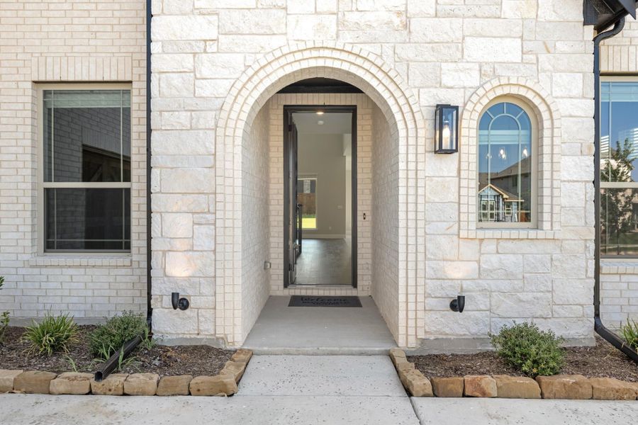 Home entrance with arched stone surround, glass front door, wall sconce, and small arched window on white brick exterior. Home entrance with arched stone surround, glass front door, wall sconce, and small arched window on white brick exterior.