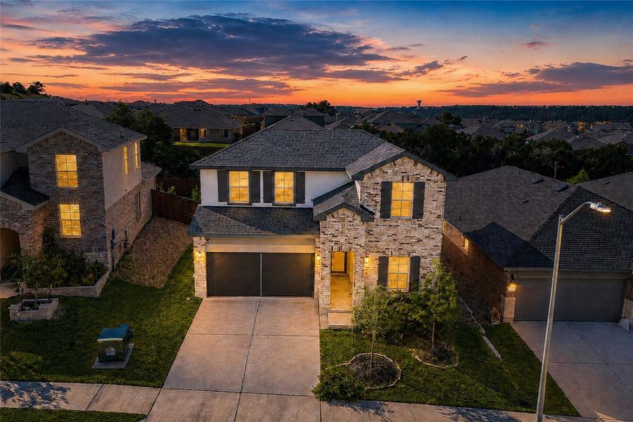 Aerial view of home at dusk featuring a striking modern home with a brick and stone facade welcomes with an inviting entryway and integrated garage.