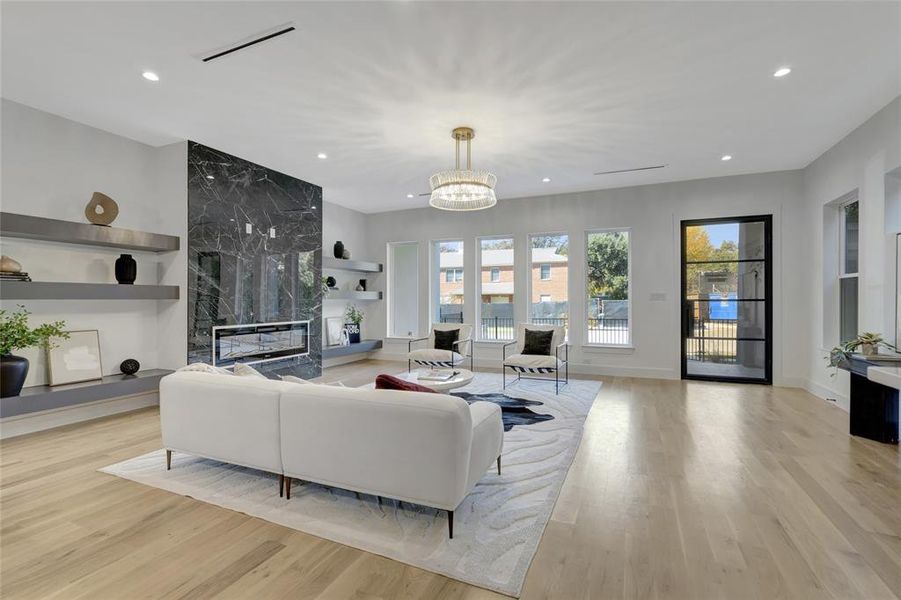 Living room with built in shelves, a fireplace, an inviting chandelier, and light hardwood / wood-style floors. Furniture is not included and is for staging only